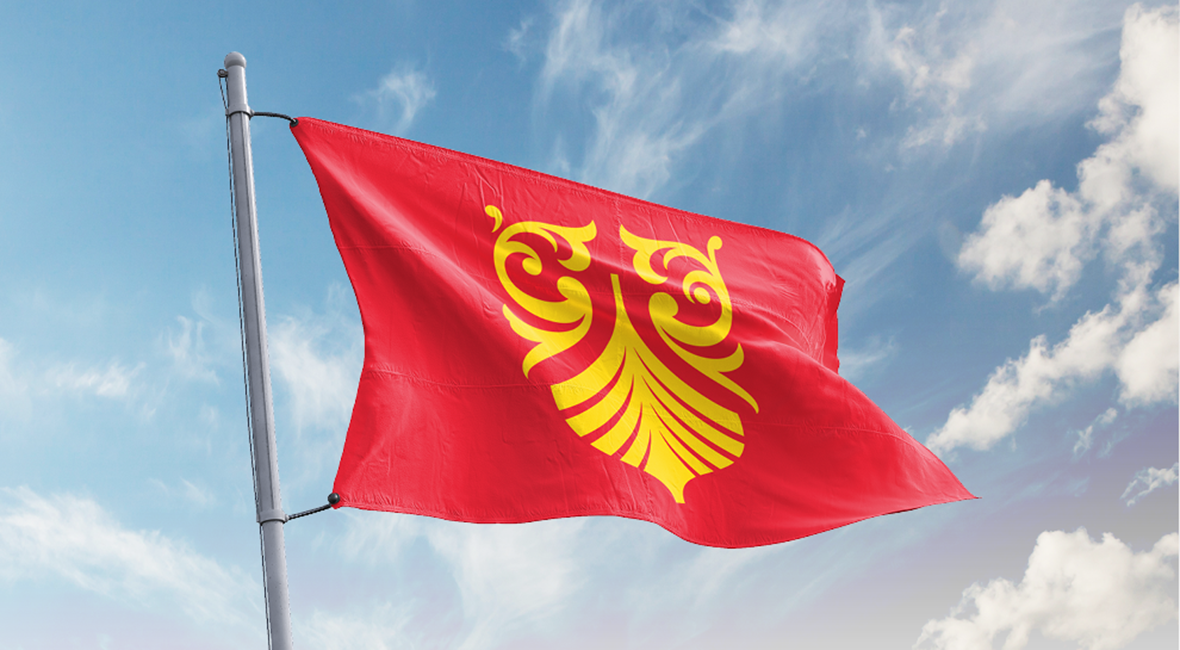 Flagg i rødt og fylkesvåpenets motiv i gult. Flagget vaier i vinden. Foto.